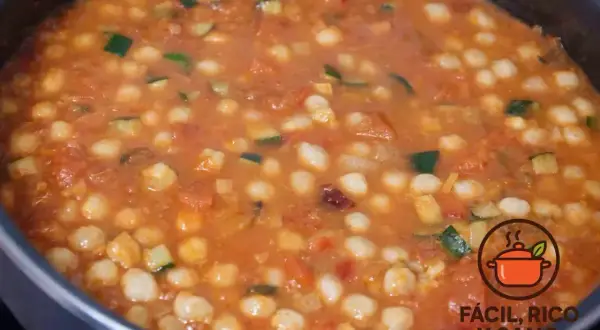 Un guiso casero de garbanzos con verduras, como calabacín y tomate, burbujeando en una olla.