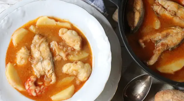 Un plato humeante de suquet de pescado, con trozos de pescado blanco, patatas y gambas en una rica salsa.