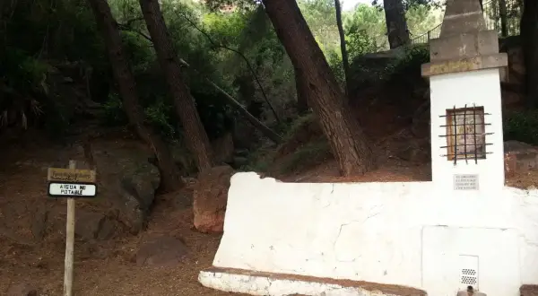 En la ruta de las fuentes, un cartel indica "AIGUA NO POTABLE" junto a una fuente de piedra y un pequeño altar en un bosque.