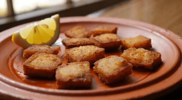 Deliciosos trozos de bacalao rebozado, dorados y crujientes, servidos en un plato de barro con una rodaja de limón.
