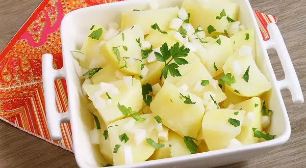 Papas aliñas recién preparadas, con trocitos de cebolla y perejil fresco, listas para disfrutar.