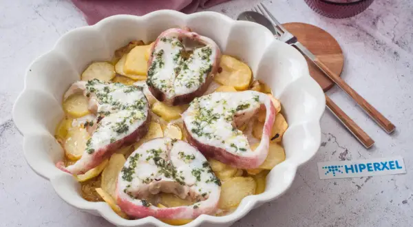 Rodajas de pescado rosado al horno con patatas, cubiertas de hierbas frescas.