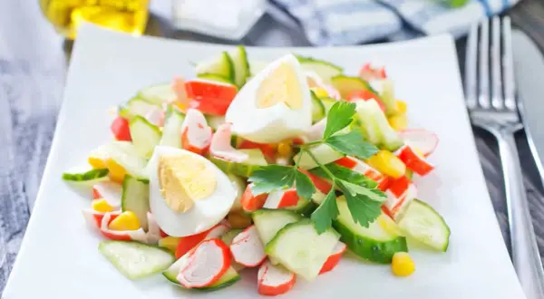 Deliciosa ensalada de cangrejo con pepino, huevo cocido y maíz, decorada con perejil fresco.