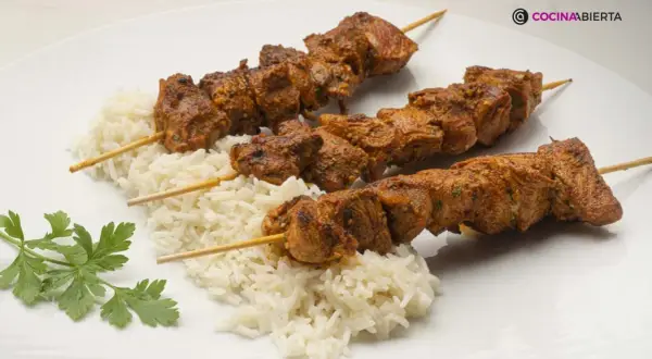 Tres pinchos morunos jugosos sobre una cama de arroz blanco, decorados con perejil fresco.