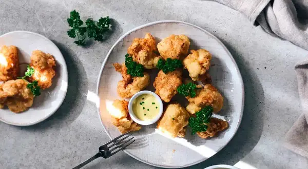 Crujiente coliflor rebozada, dorada y servida con salsa de mostaza y perejil fresco. ¡Un aperitivo delicioso!