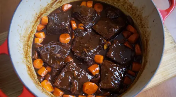 Boeuf bourguignon cocinado a fuego lento en una olla roja, con trozos de carne tierna, zanahorias y champiñones en una rica salsa.
