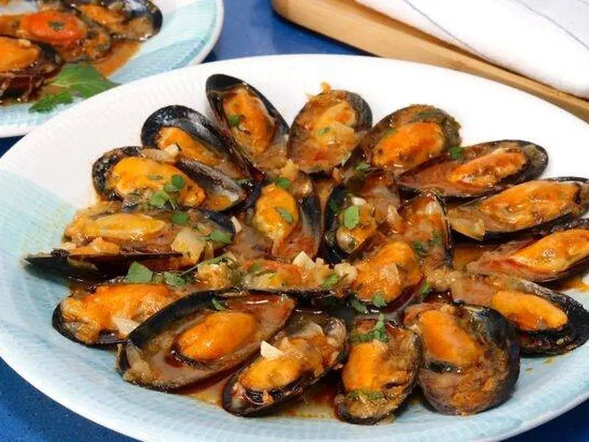 Un plato de mejillones a la marinera, jugosos y con una salsa sabrosa, adornados con perejil fresco.