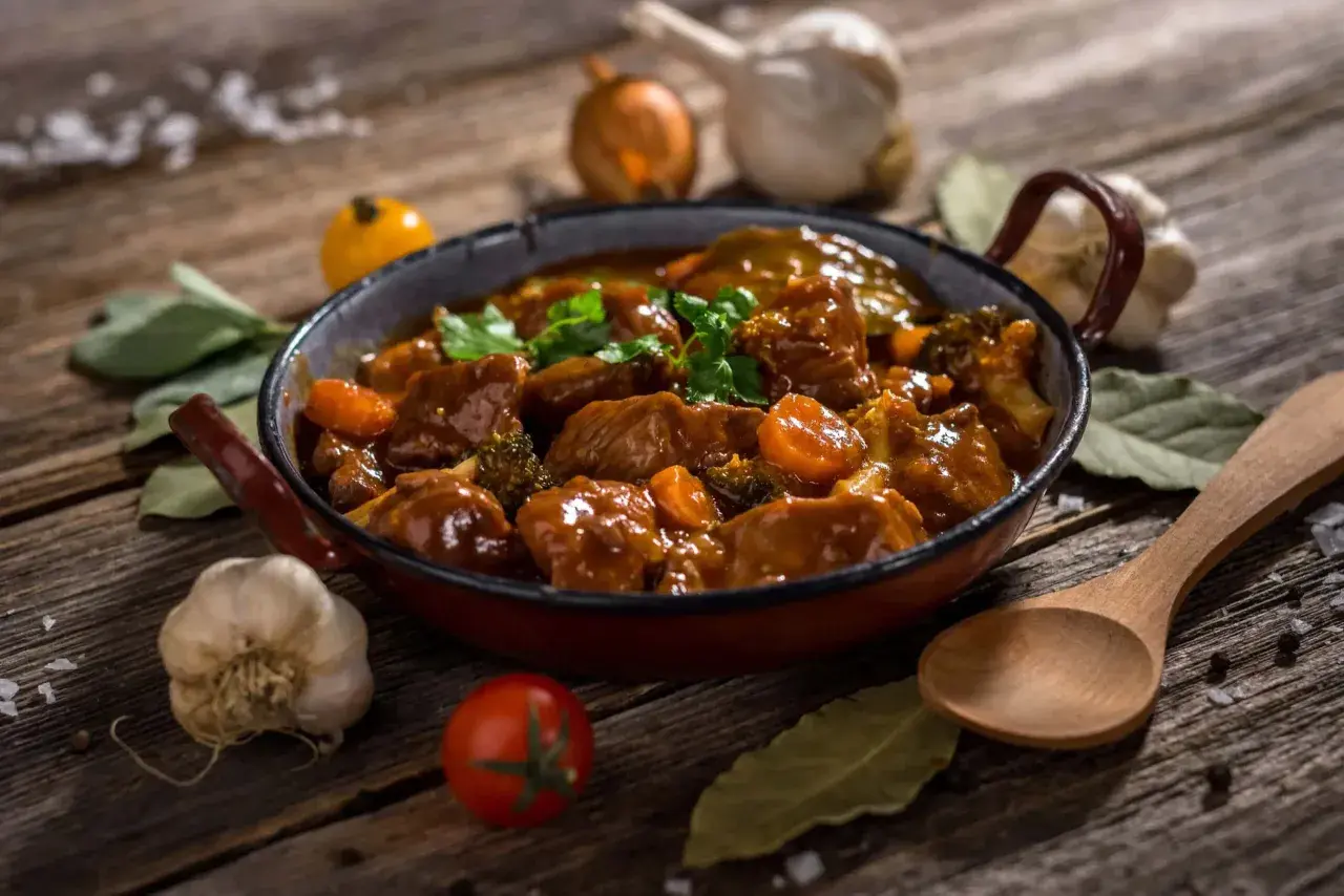 Un delicioso ragout de ternera, con trozos de zanahoria y brócoli, servido en una sartén rústica. Acompañado de ajo, tomate y laurel.