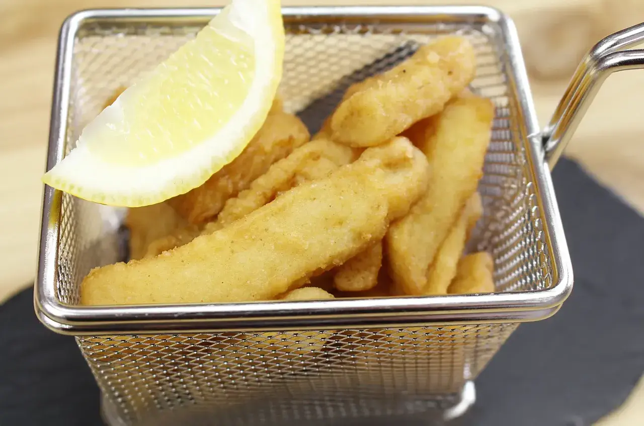 Deliciosos chocos fritos crujientes en una cesta metálica, acompañados de una rodaja de limón.