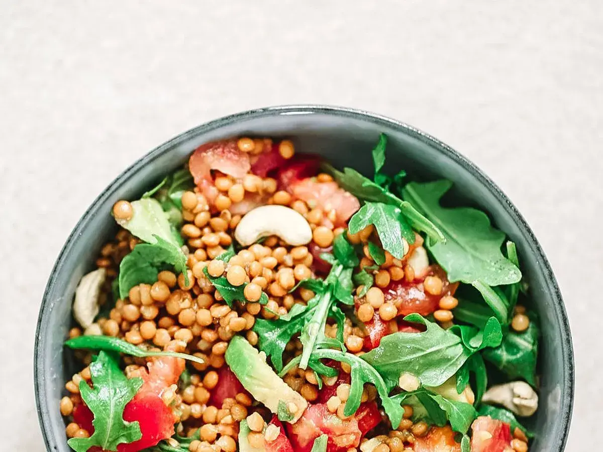 Deliciosa ensalada de lentejas con aguacate, tomate y rúcula, coronada con anacardos. Un plato fresco y nutritivo.