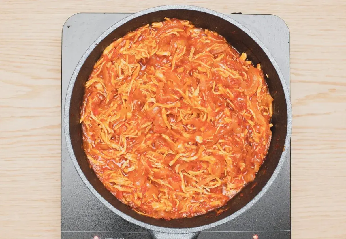 Tinga de pollo cocinándose en una sartén, con trozos de pollo deshebrado y salsa roja.