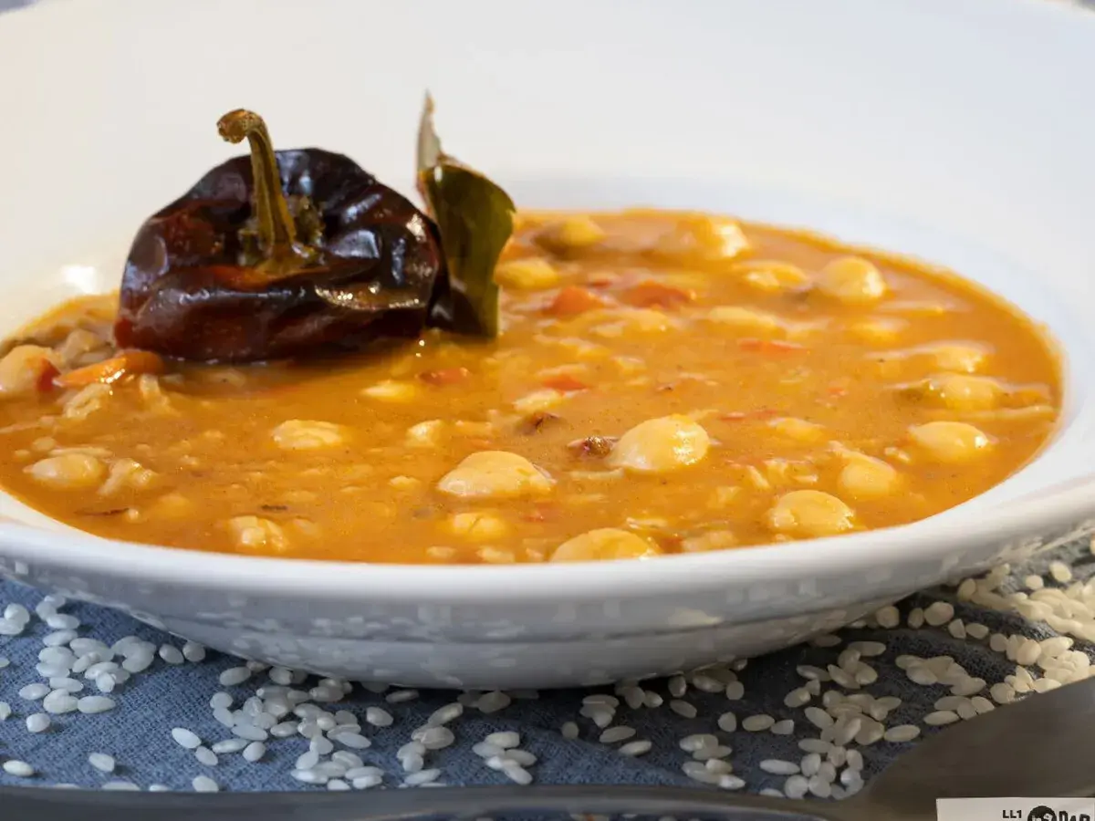 Un plato humeante de garbanzos con arroz, decorado con un pimiento seco y una hoja de laurel.