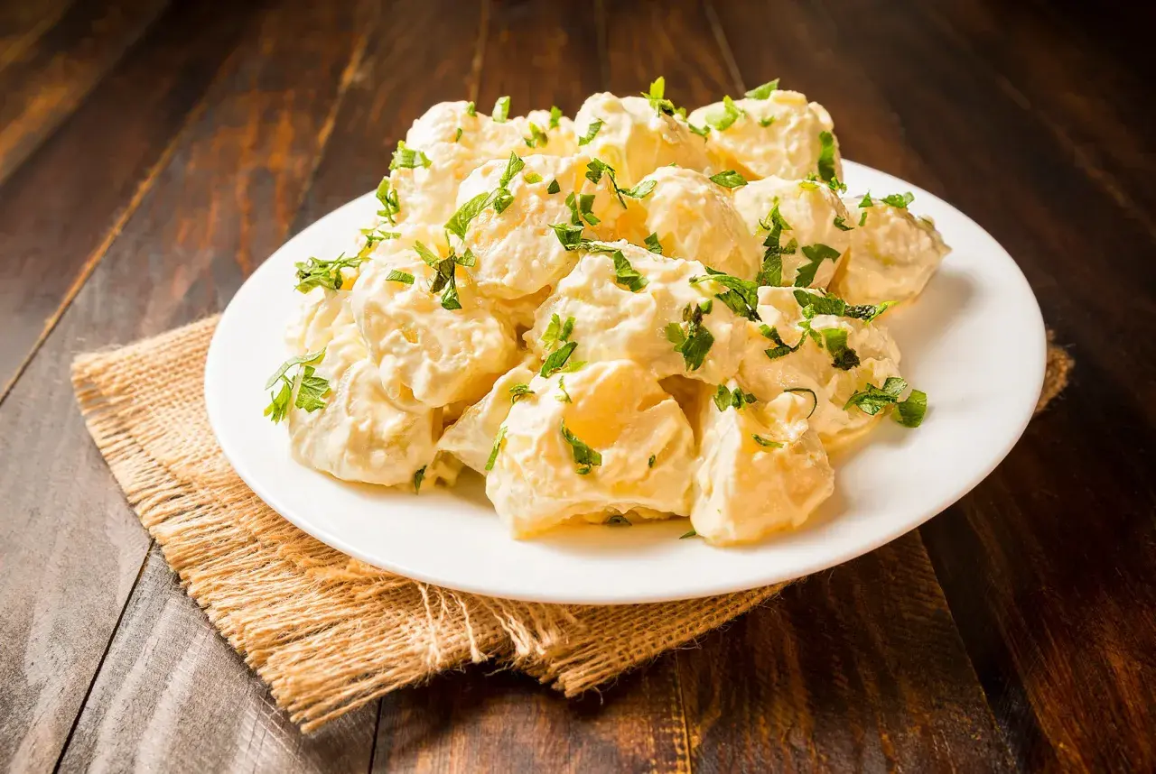 Patatas alioli cremosas y deliciosas, cubiertas con perejil fresco, servidas en un plato blanco sobre una mesa de madera rústica.