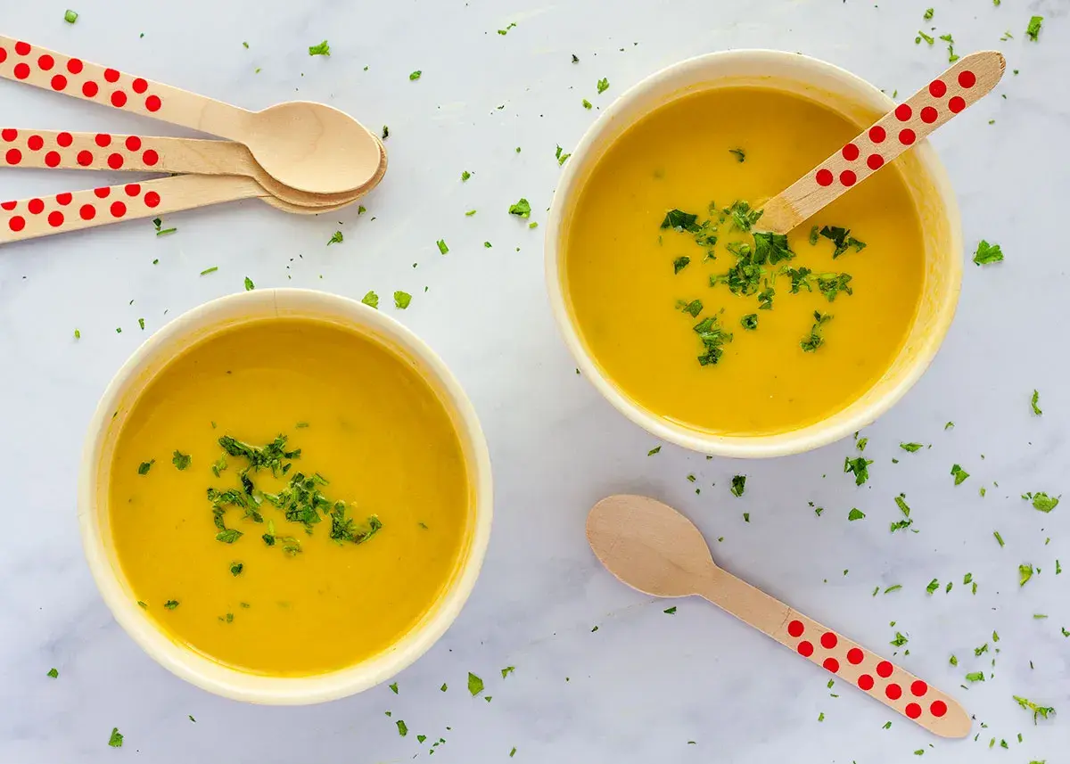 Dos cuencos de cremoso pure de verduras, decorados con perejil picado y cucharas de madera con lunares rojos.