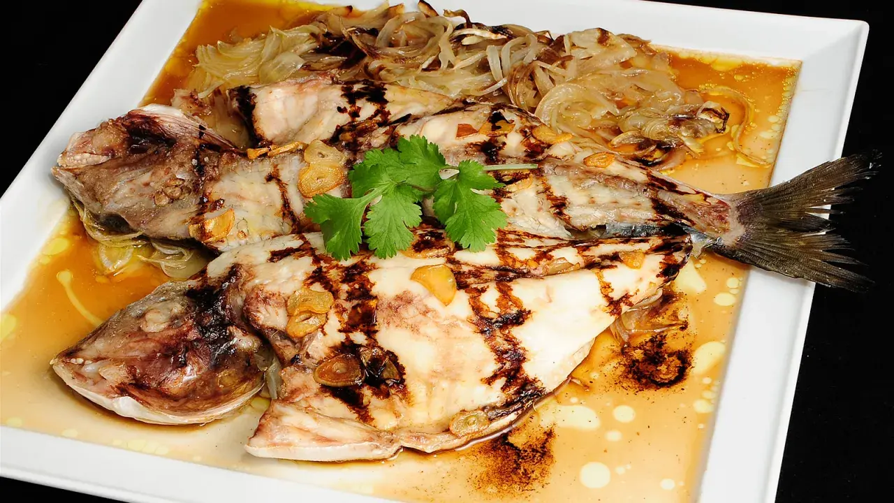 Dorada a la espalda, jugosa y a la parrilla, servida con cebolla caramelizada, ajo y cilantro fresco en una salsa dorada.