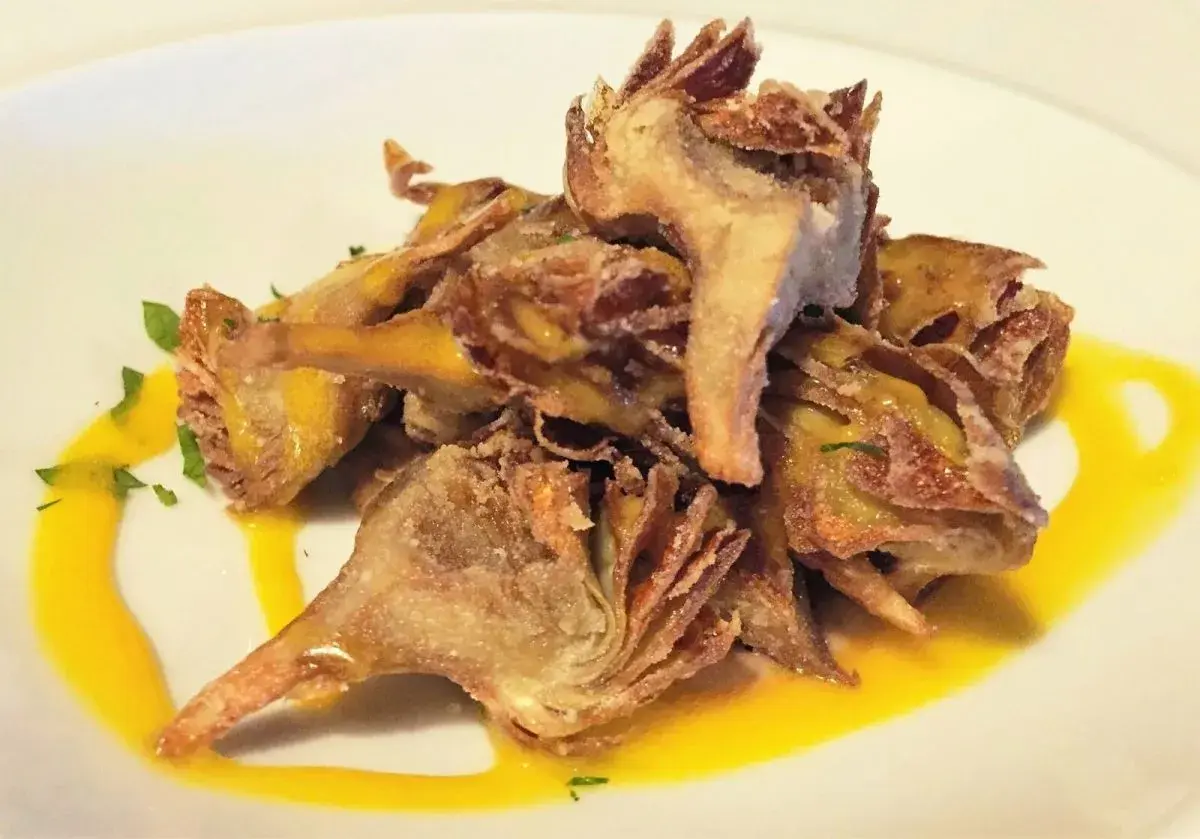 Deliciosas alcachofas fritas crujientes, servidas con una salsa dorada y perejil picado.