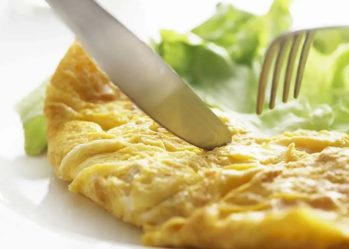 Un cuchillo corta una dorada tortilla francesa junto a hojas de lechuga fresca.
