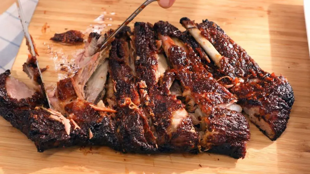 Costillas a la barbacoa jugosas y tiernas, cortadas en una tabla de madera. La carne se desprende del hueso, cubierta de salsa.