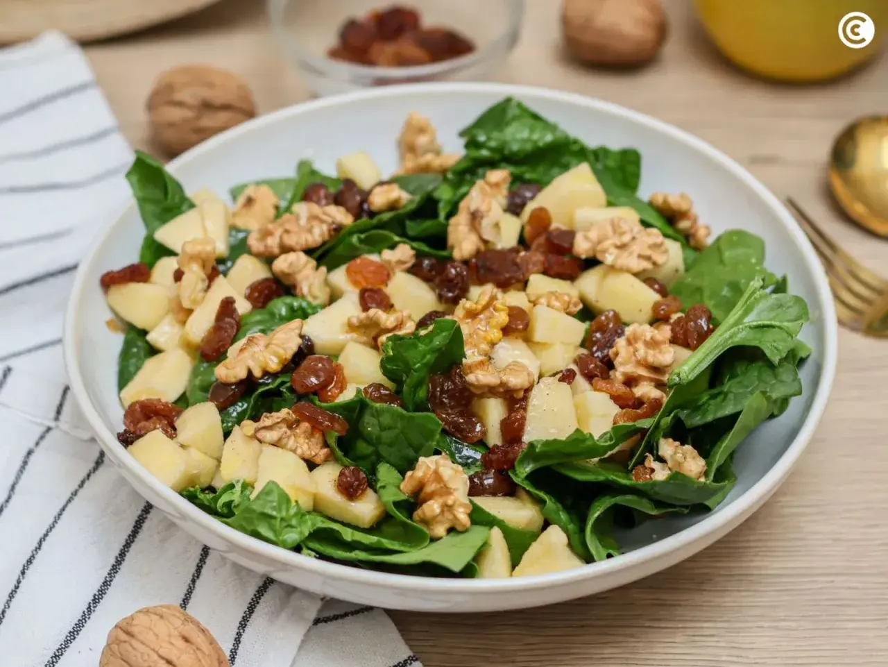 Deliciosa ensalada de espinacas con trozos de manzana, pasas y nueces crujientes. Un festín de texturas y sabores.