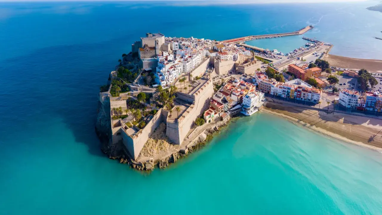 Castellón Costa Azahar: un pueblo amurallado con un castillo se alza sobre el mar turquesa, con un puerto deportivo y playas doradas.
