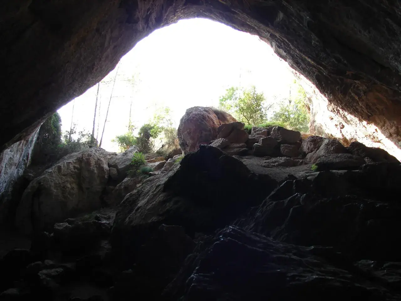 Salida de la cueva negra Montanejos, con rocas y vegetación iluminadas por el sol.