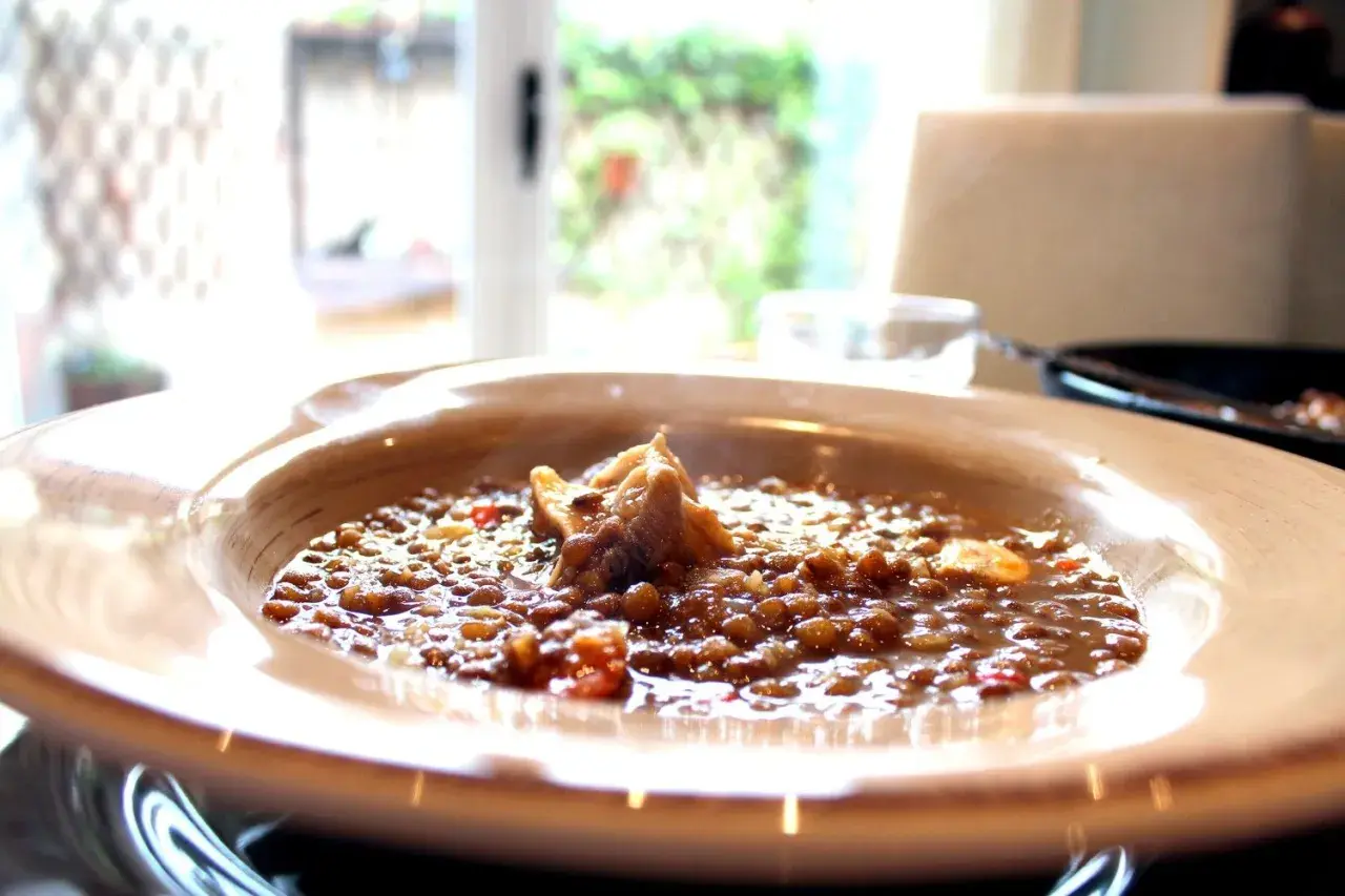 Un plato humeante de lentejas con chorizo, servido en un cuenco de madera, con un trozo de carne en el centro.