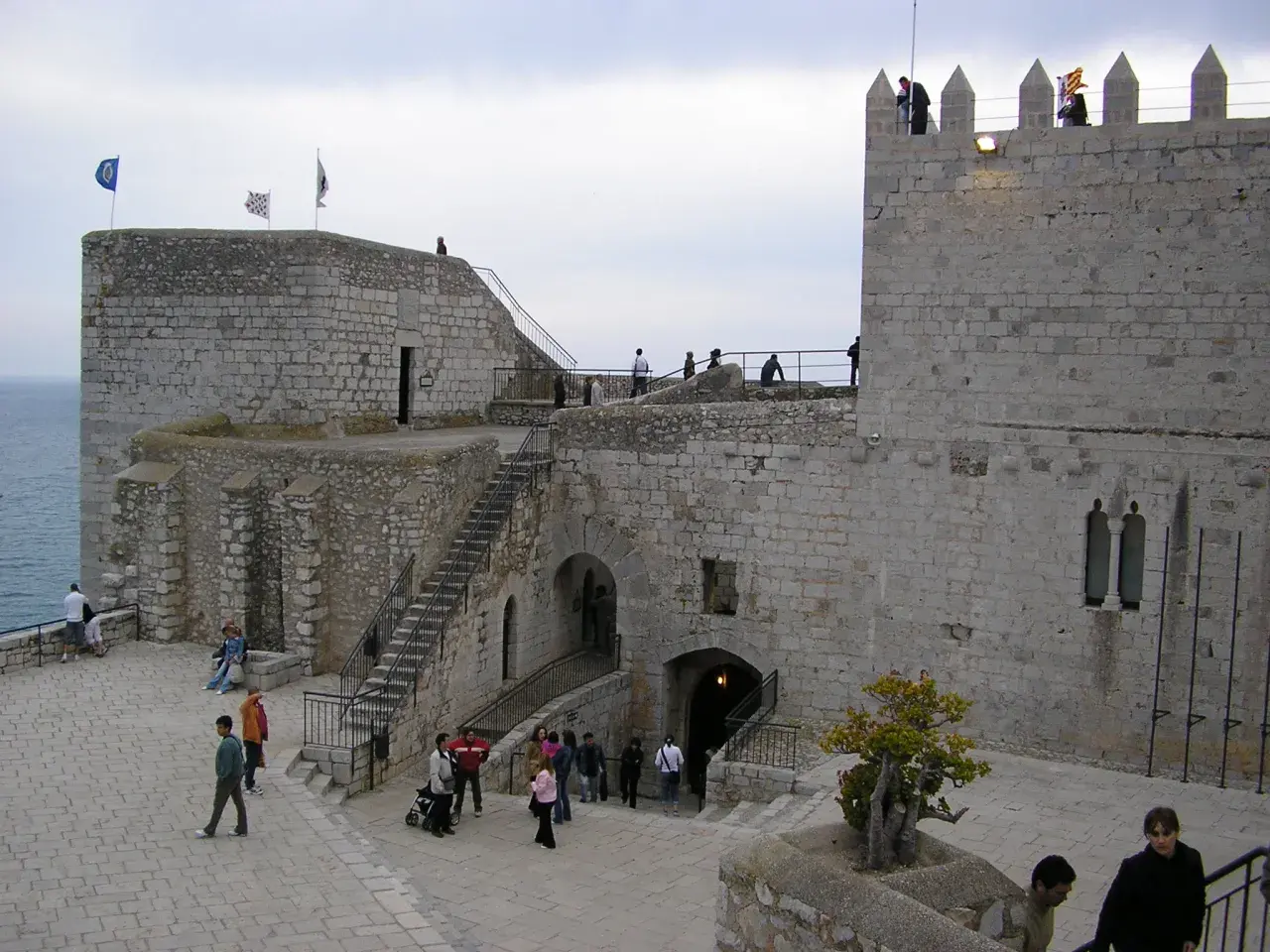 El castillo de Peñíscola se alza imponente sobre el mar. Turistas pasean por sus patios de piedra, admirando la arquitectura histórica.