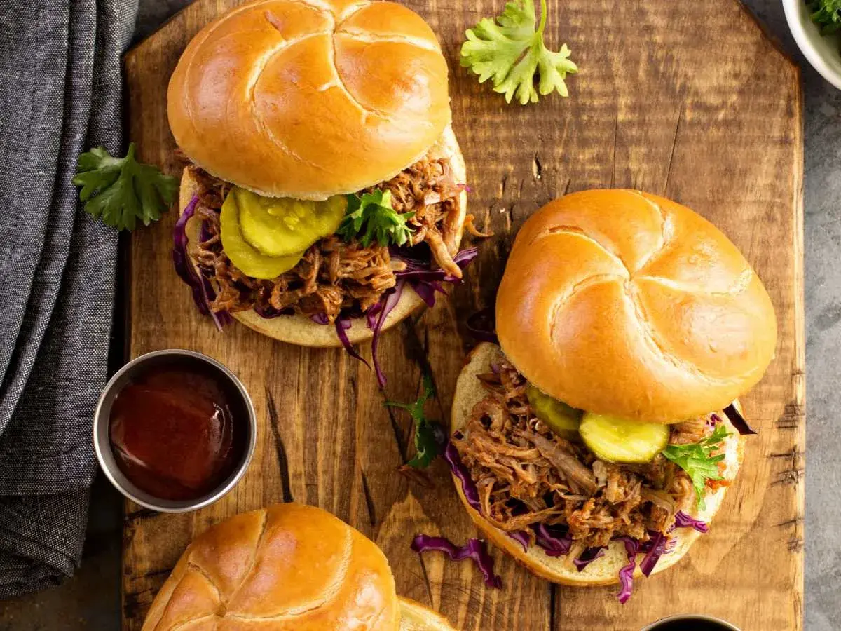 Dos jugosos sándwiches de pulled pork con pepinillos y col morada sobre pan rústico, listos para disfrutar.
