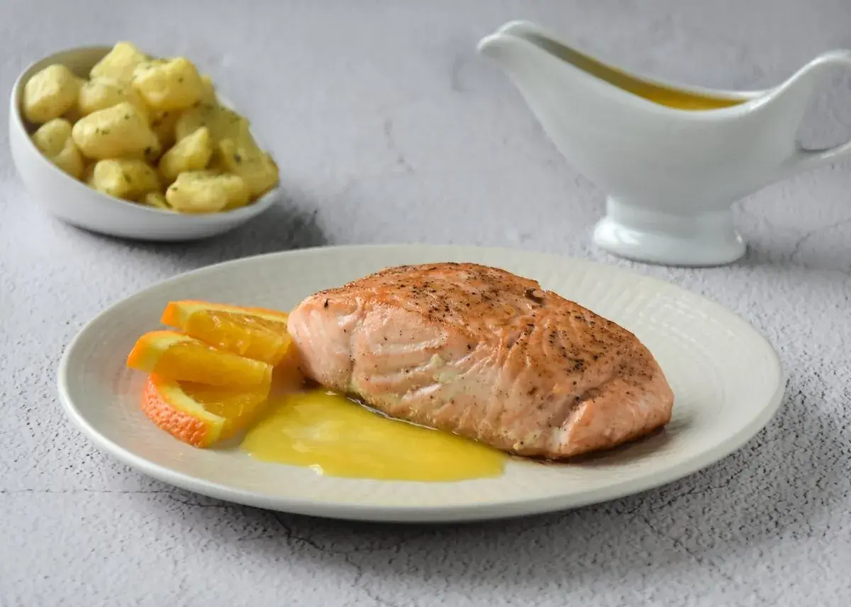 Filete de salmón a la naranja, servido con gajos de naranja y una salsa dorada. Acompaña unas patatas.