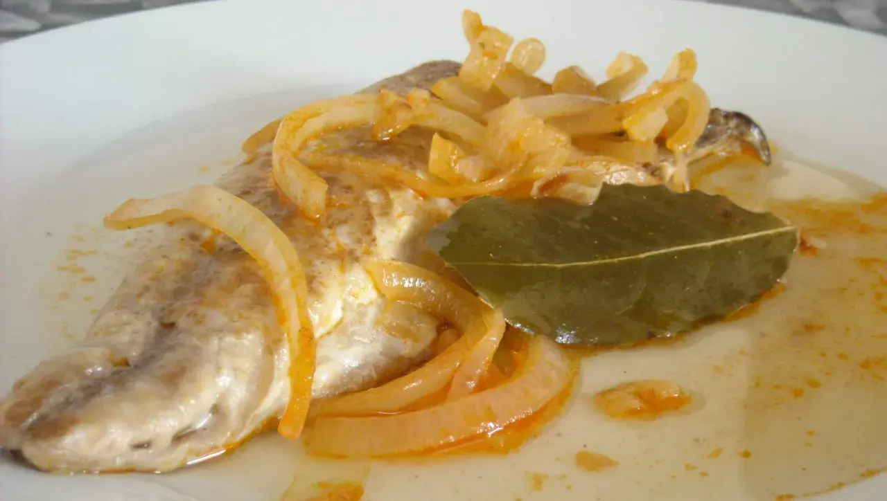 Deliciosa caballa en escabeche, con cebolla caramelizada y hoja de laurel, servida en un plato blanco.