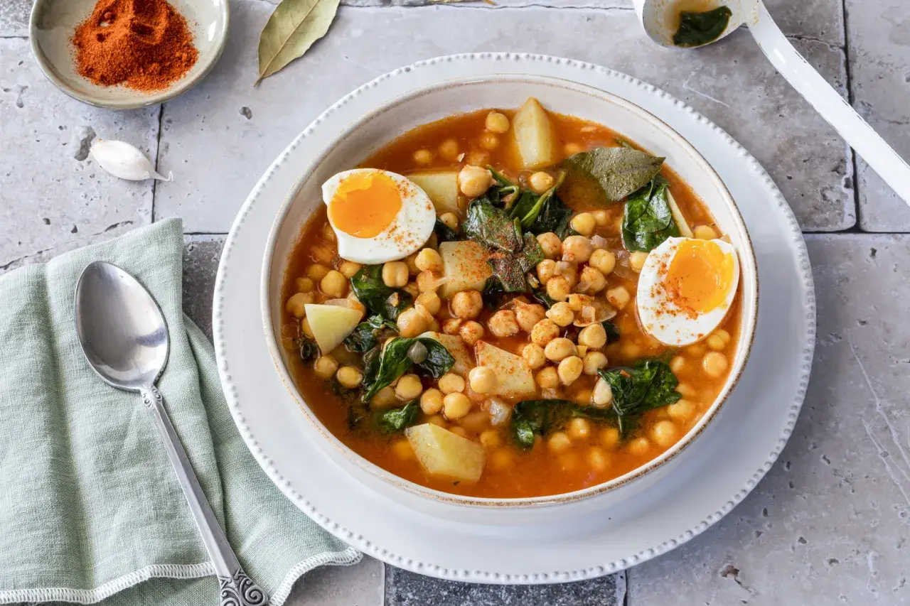 Un reconfortante plato de garbanzos con espinacas, patatas y huevos duros, espolvoreado con pimentón.
