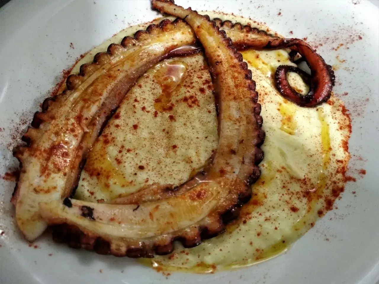 Tentáculos de pulpo a la plancha, dorados y tiernos, servidos sobre puré cremoso y espolvoreados con pimentón.