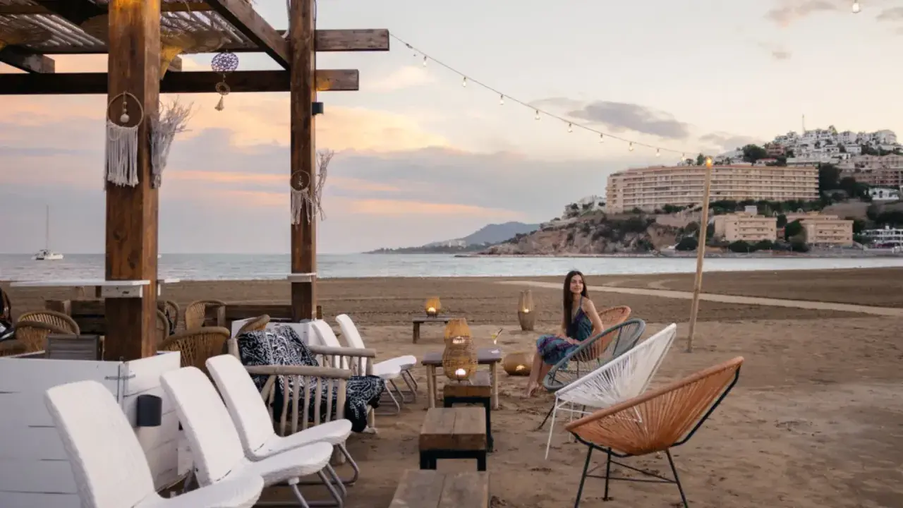 Una mujer disfruta de la tarde en la playa sur Peñíscola, sentada en una silla de diseño frente al mar.