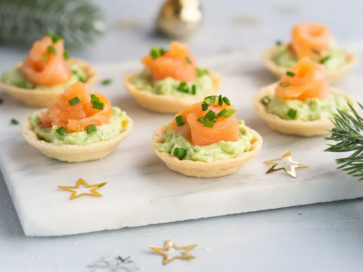Aperitivos baratos para mucha gente: tartaletas crujientes con aguacate cremoso y salmón ahumado, decoradas con cebollino. ¡Perfectas para fiestas!