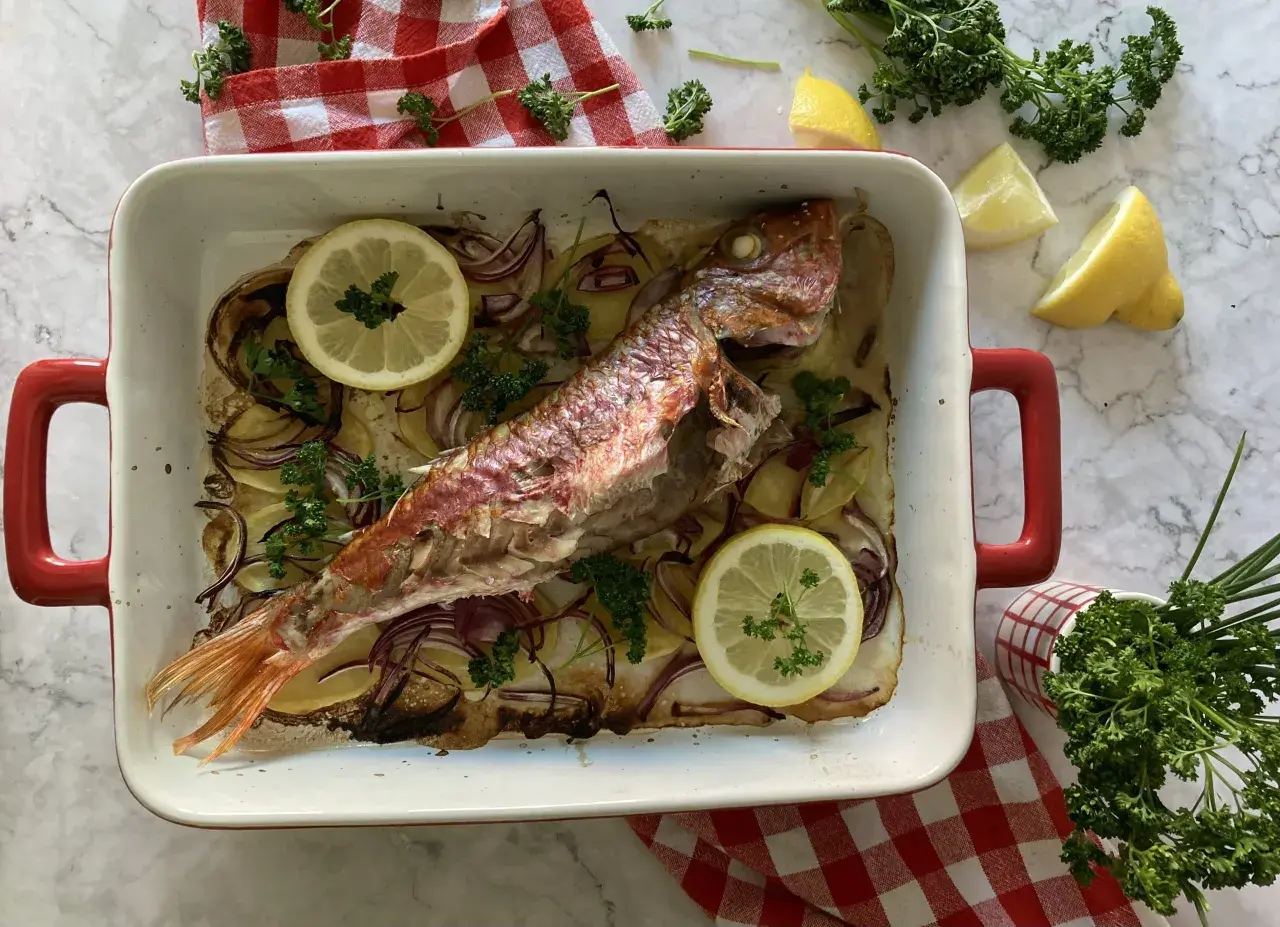 Deliciosos salmonetes al horno con patatas, cebolla roja, limón y perejil fresco, listos para servir.