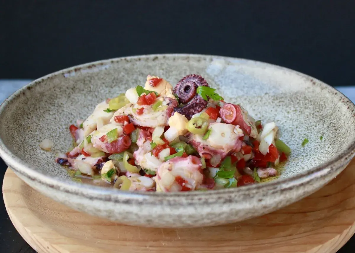 Salpicon de pulpo fresco con pimientos, cebolla y perejil, servido en un cuenco rústico.