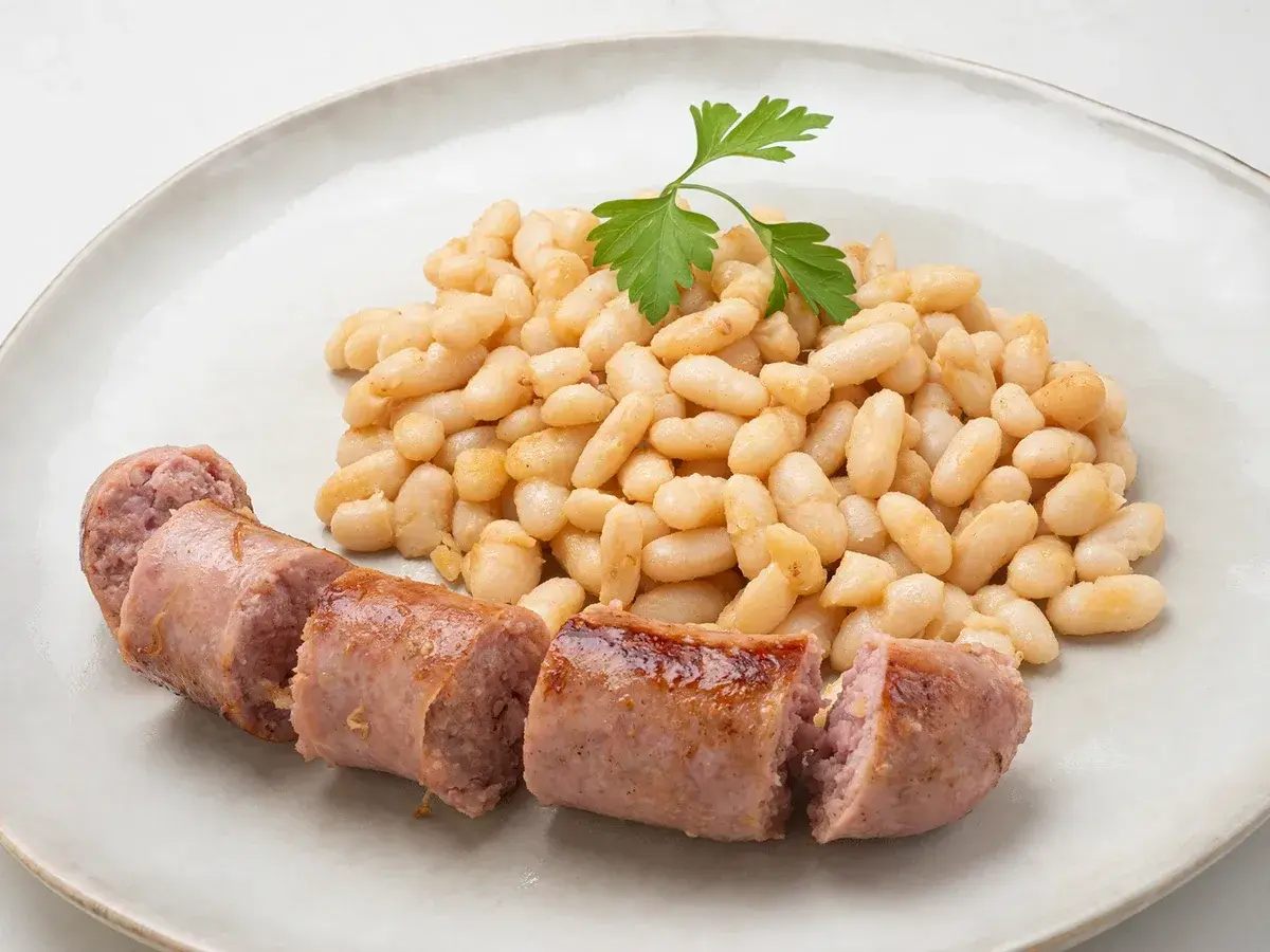 Un plato de alubias blancas tiernas y jugosas salchichas, decorado con una ramita de perejil fresco.