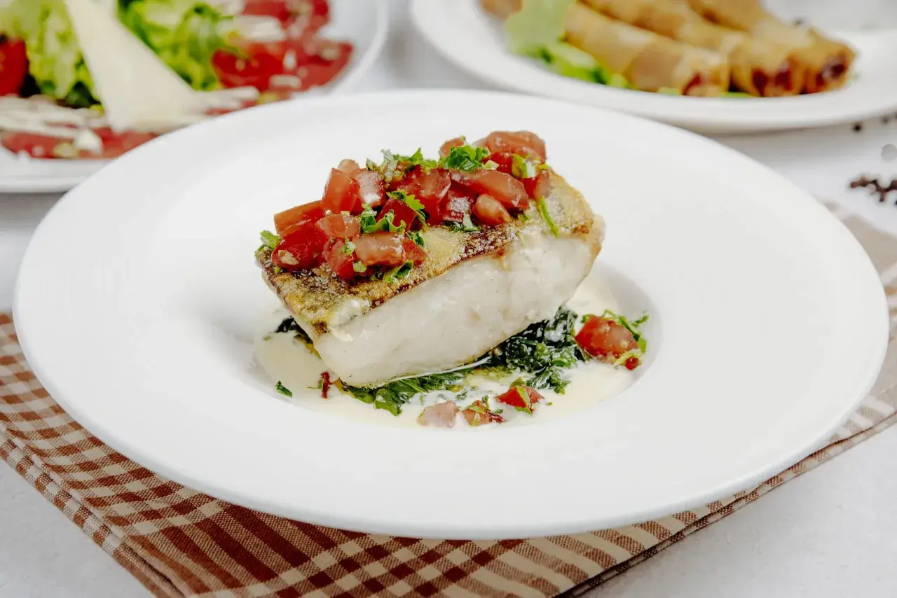 Filete de bacalao con tomate y hierbas, sobre espinacas y salsa cremosa. Un plato principal ideal para tus recetas de bacalao.