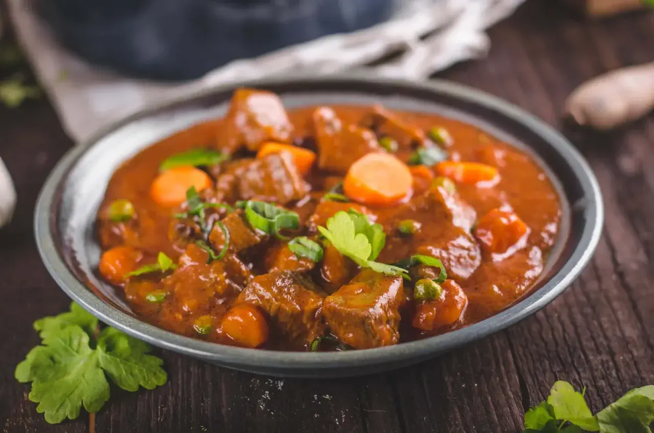 Un plato humeante de rabo de ternera estofado con zanahorias y guisantes, adornado con perejil fresco.
