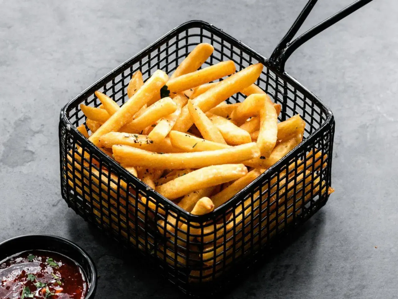 Patatas soufflé doradas y crujientes en una cesta negra, listas para ser disfrutadas con una salsa.