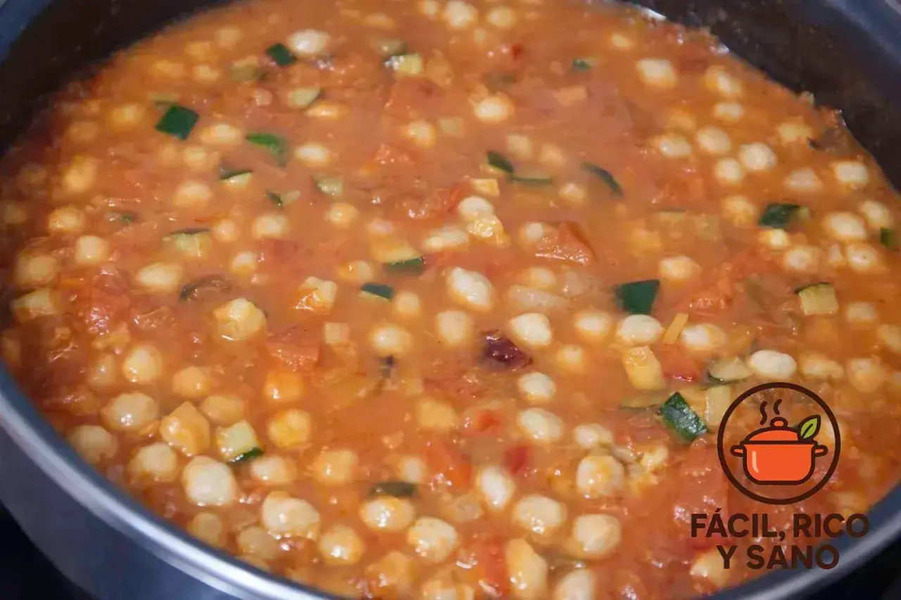 Un guiso casero de garbanzos con verduras, como calabacín y tomate, burbujeando en una olla.