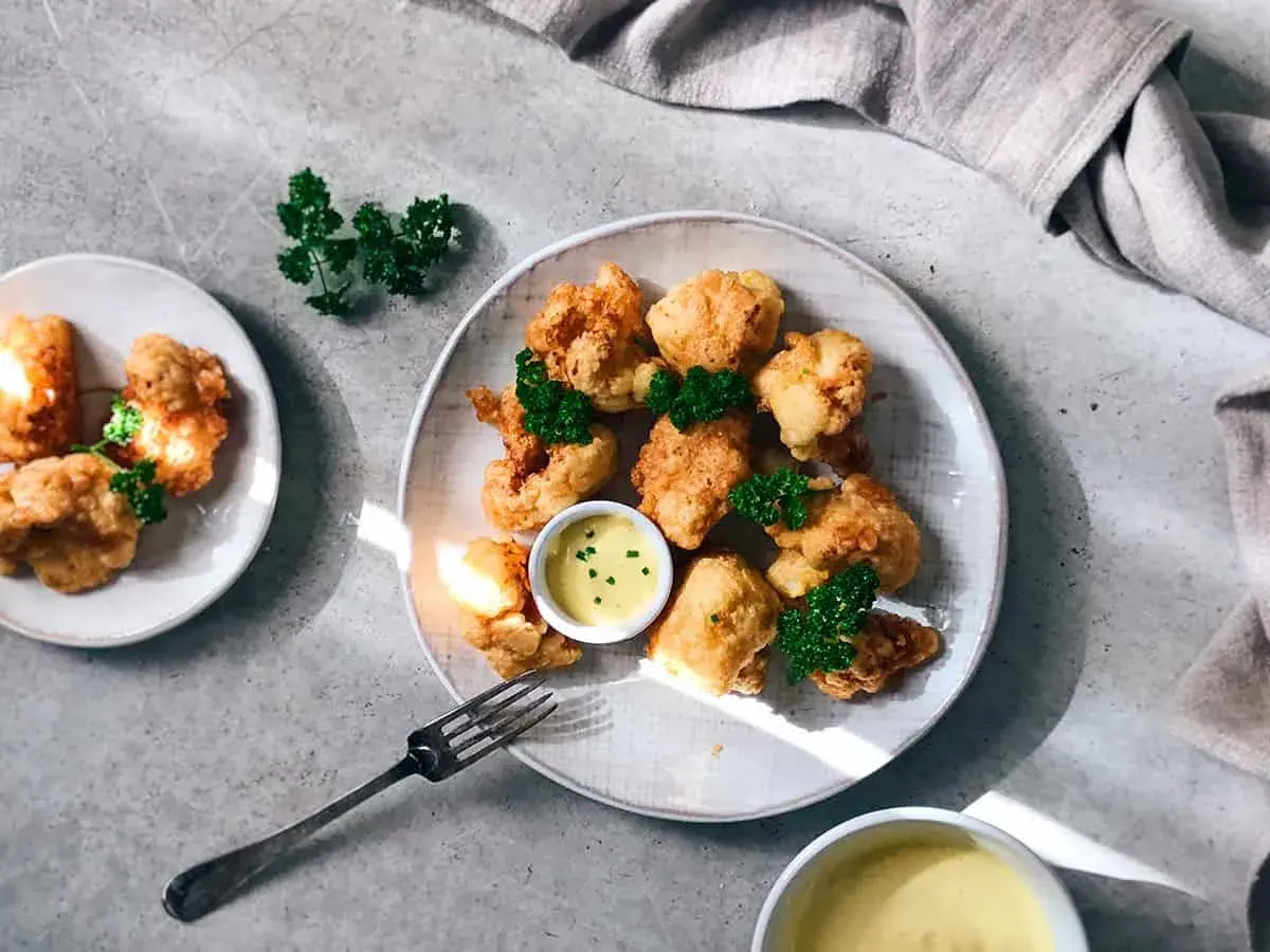 Crujiente coliflor rebozada, dorada y servida con salsa de mostaza y perejil fresco. ¡Un aperitivo delicioso!