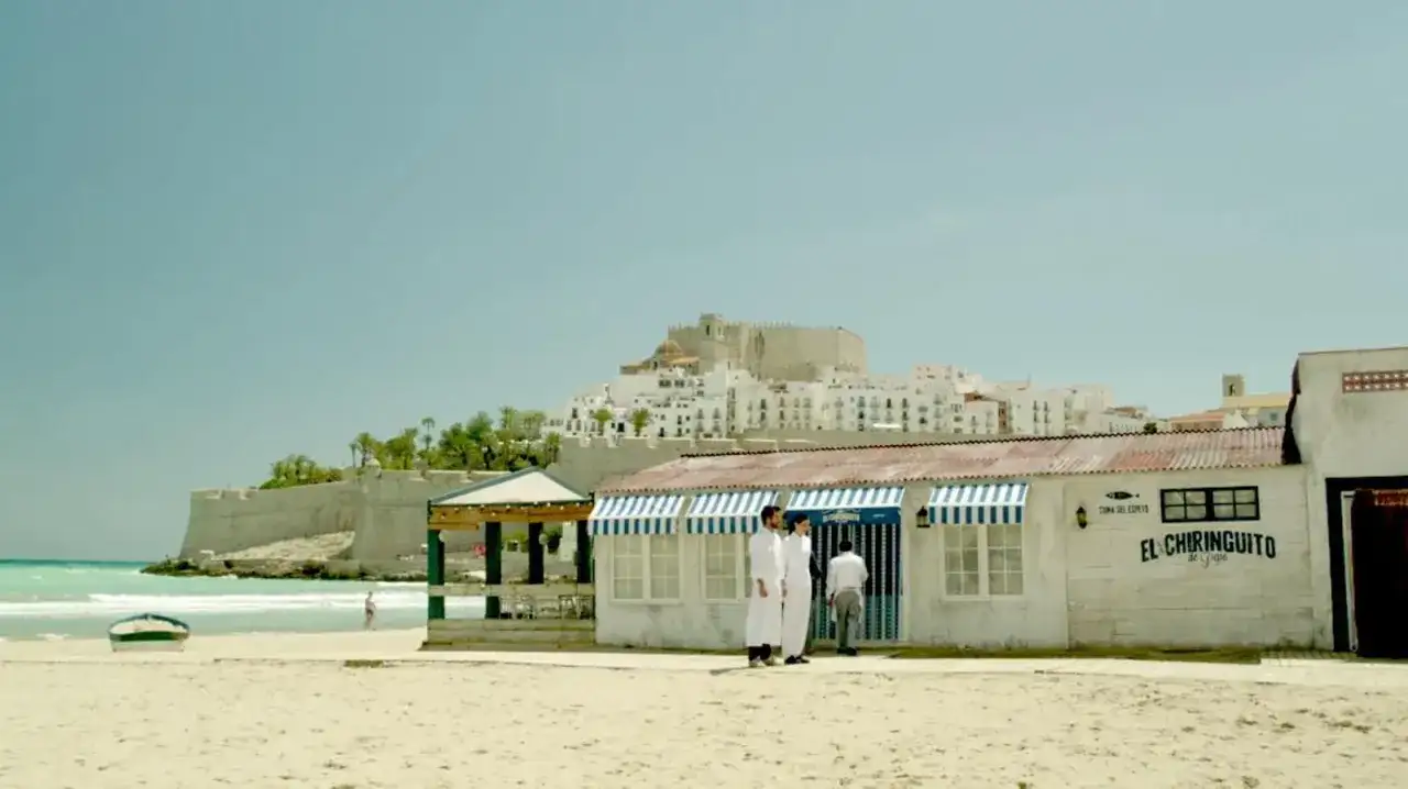 El chiringuito de Pepe, un restaurante playero con vistas a un pueblo blanco y un castillo.