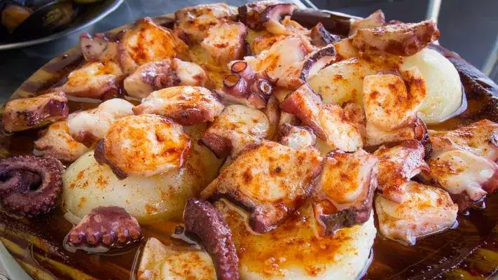 Pulpo a la gallega servido en plato de madera, con patatas cocidas y espolvoreado con pimentón.