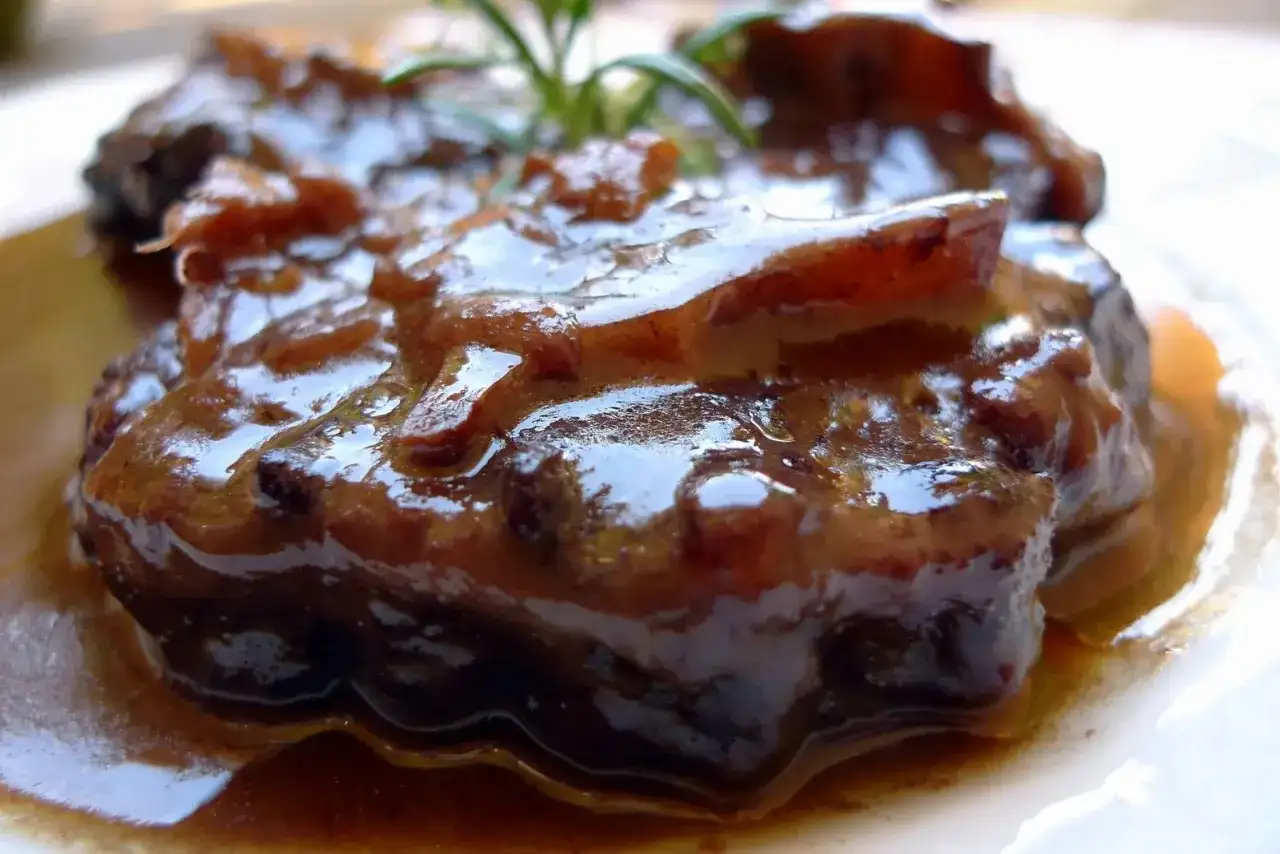 Un plato de rabo de toro estofado, jugoso y cubierto de una rica salsa oscura. Una ramita de romero decora la carne.