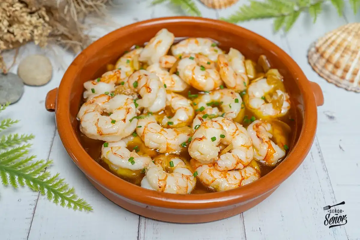 Un plato de gambas al ajillo burbujeantes en una cazuela de barro, adornado con perejil picado.