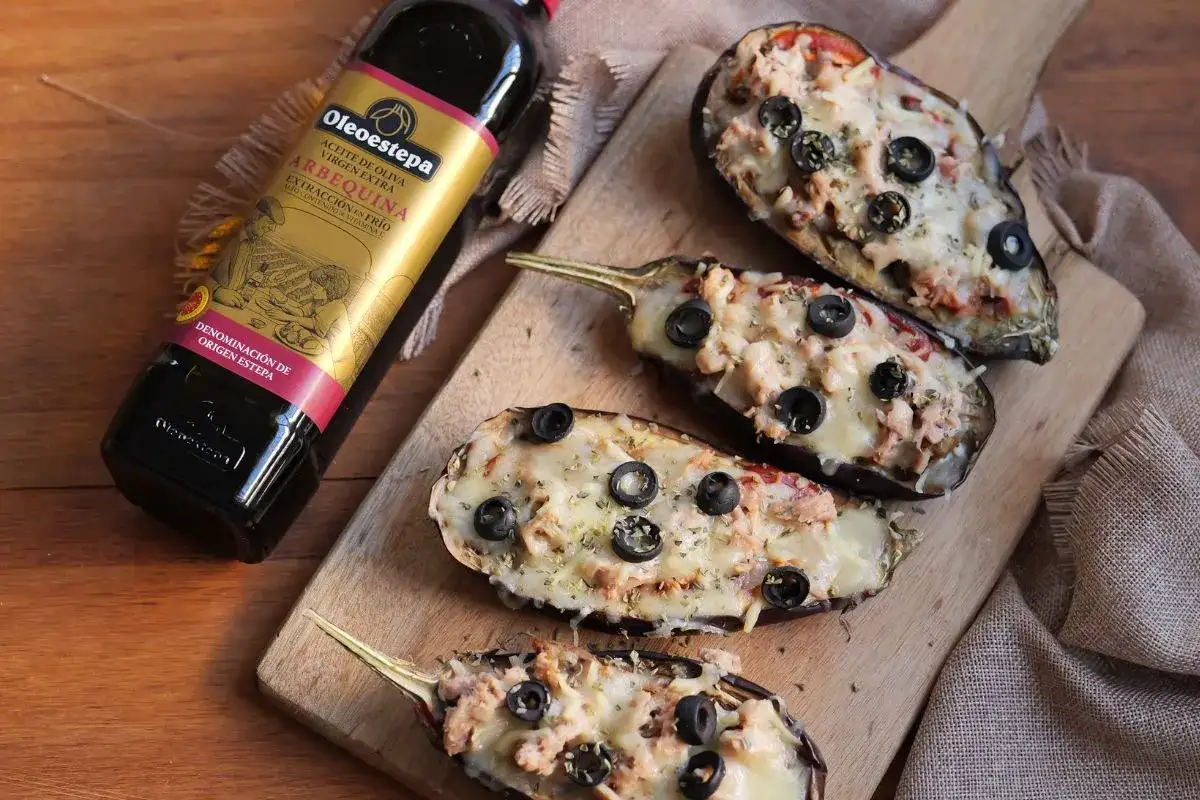 Berenjenas rellenas gratinadas con queso y aceitunas, junto a una botella de aceite de oliva virgen extra Oleoestepa.