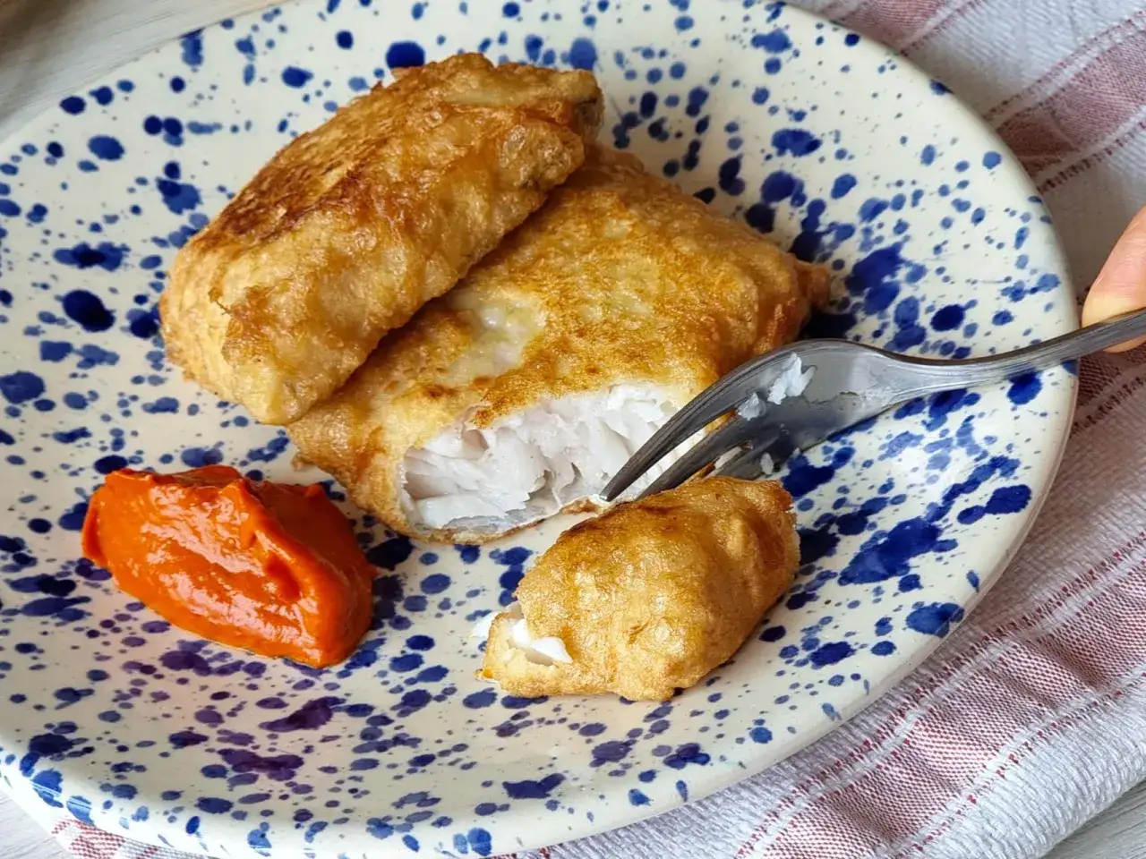Deliciosa merluza a la romana, crujiente por fuera y jugosa por dentro, servida con una salsa de pimientos.