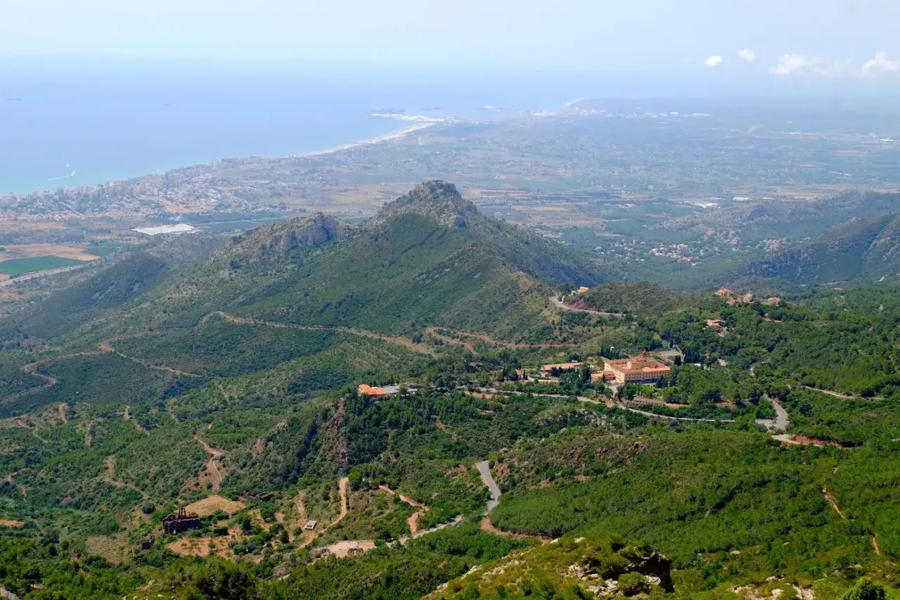 Vista panor&aacute;mica del desierto de las Palmas, con el mar Mediterr&aacute;neo al fondo y edificios hist&oacute;ricos entre la vegetaci&oacute;n.