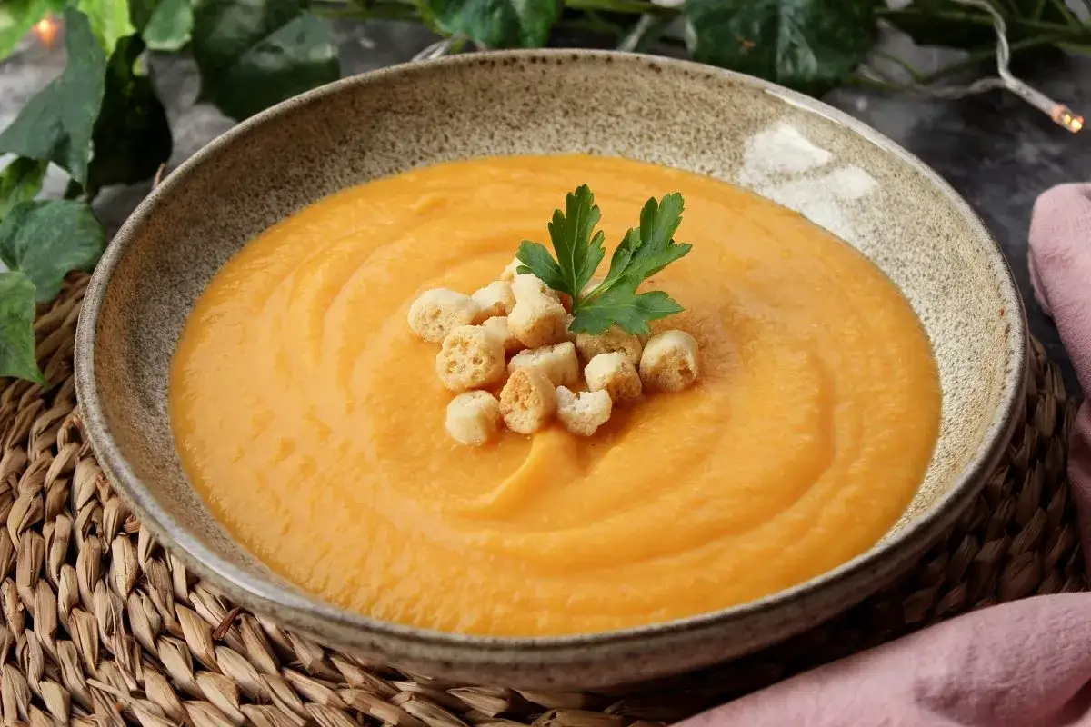Un reconfortante pur&eacute; de verduras cremoso, adornado con picatostes crujientes y perejil fresco, servido en un cuenco r&uacute;stico.